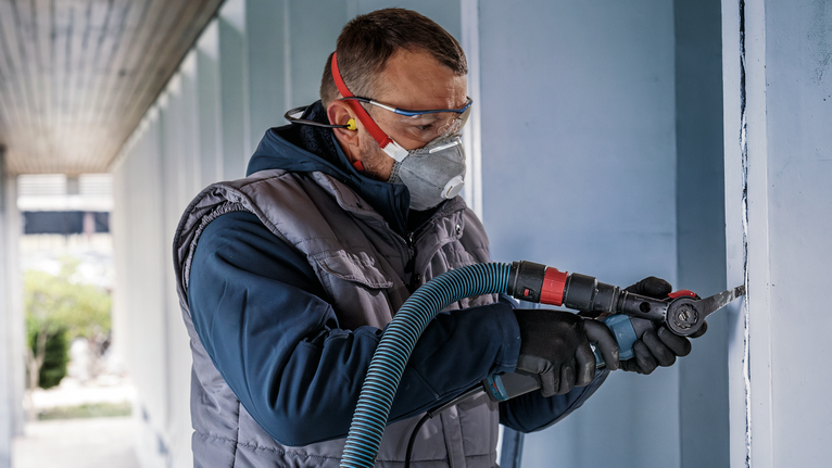 配戴安全設備的人員使用電動工具切割牆壁。