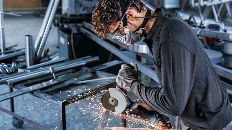 配戴安全設備的人使用角磨機切割金屬，產生火花。