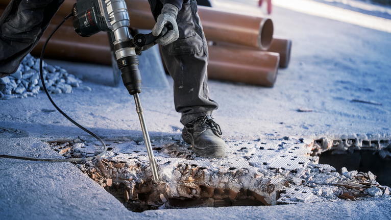 配戴安全設備的人員用破碎錘打破混凝土地板。