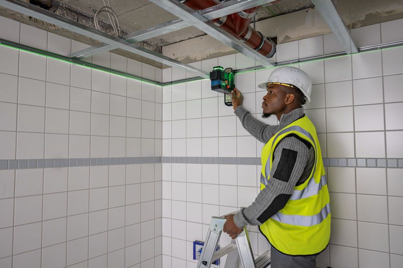 佩戴安全設備的人員從梯子上將雷射調平工具安裝在瓷磚牆上。.