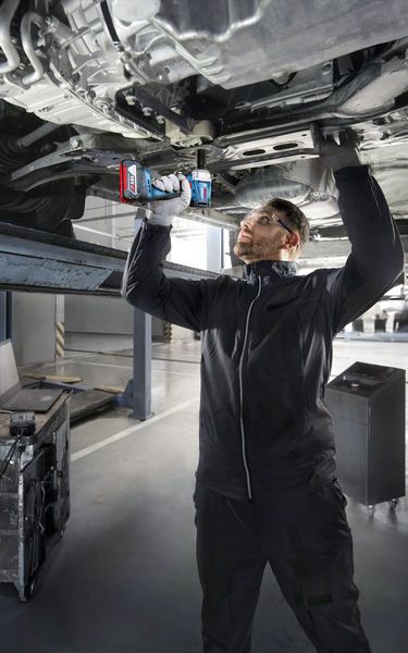 一名配戴安全設備的人員使用電鑽在升起的車輛下方作業。.