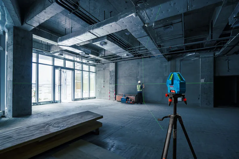 在建築工地上，一名配戴安全設備的人員正在使用雷射調平工具調整牆壁。.