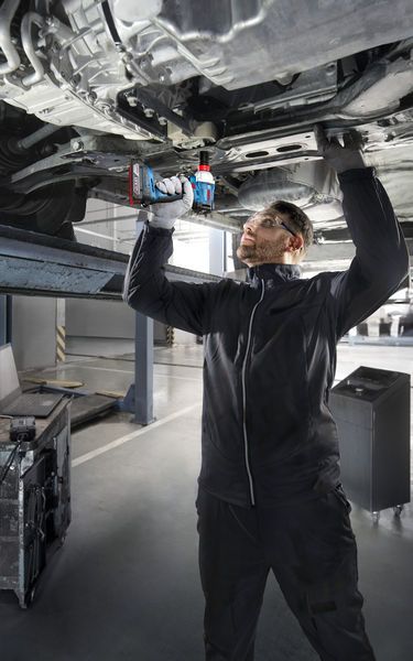 一名配戴安全設備的人員在升起的車輛下方使用無線電鑽。.