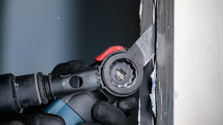 一名配戴安全設備的人員使用電動工具切割牆壁附近的材料。