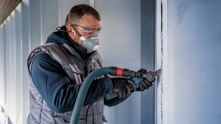 配戴安全設備的人員使用電動工具在牆上磨出垂直凹槽。