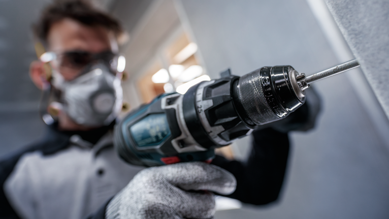 配戴安全設備的人員使用電動工具在牆上鑽孔。