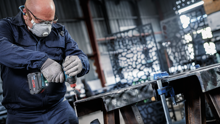 一名配戴安全設備的人員在工業車間內鑽入金屬梁。