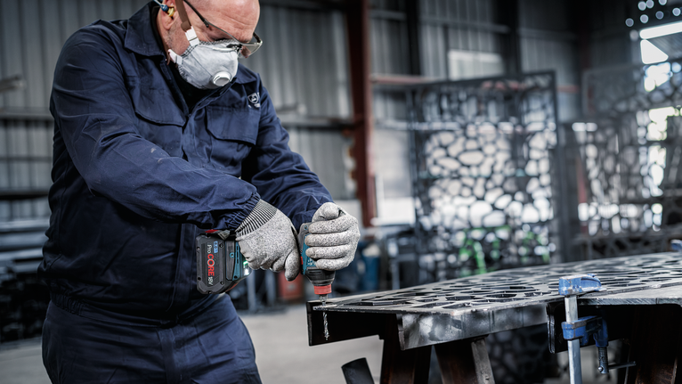 一名配戴安全設備的人員在車間內鑽金屬板。