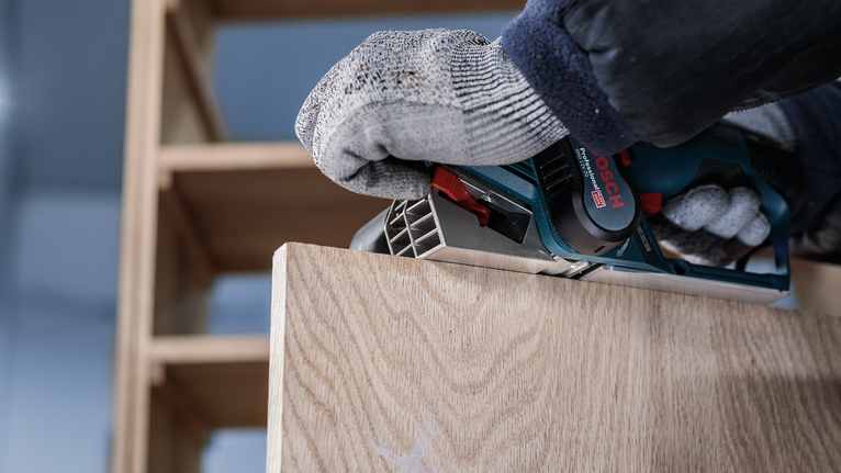 配戴安全設備的人員使用電動刨床刨削木板。