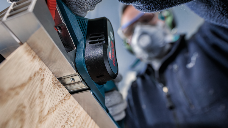 配戴安全設備的人員使用電動刨床刨削木板。