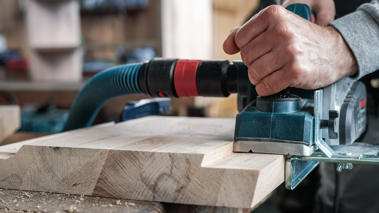 一名工人在車間使用電刨刨平木板。