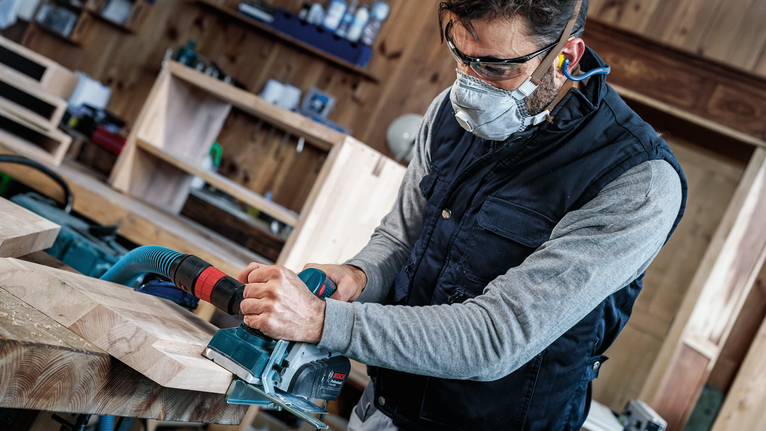 配戴安全設備的人員使用電刨來打磨木板。