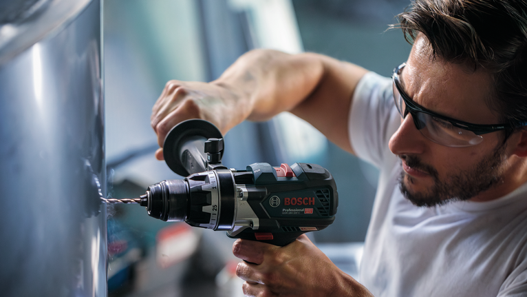 一名配戴安全設備的人使用電動工具鑽入金屬。