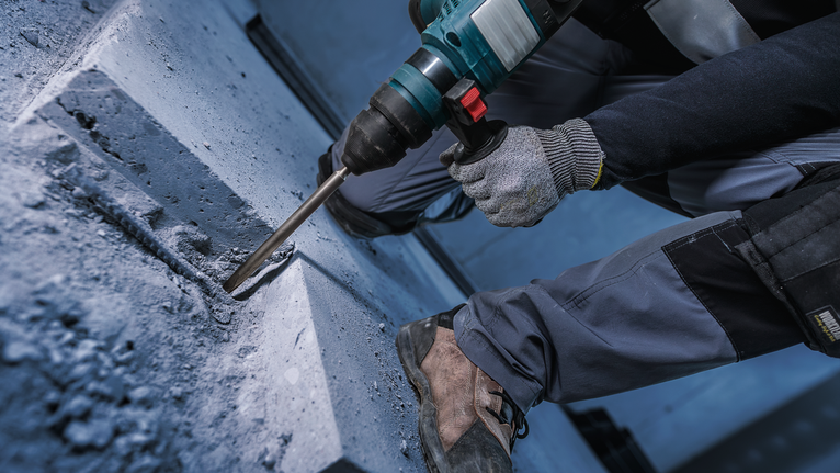 PRO SDS plus-4C 鑿子尖角鑿刀,160 mm 一名配戴安全設備的人員使用旋轉錘在混凝土中鑽孔。