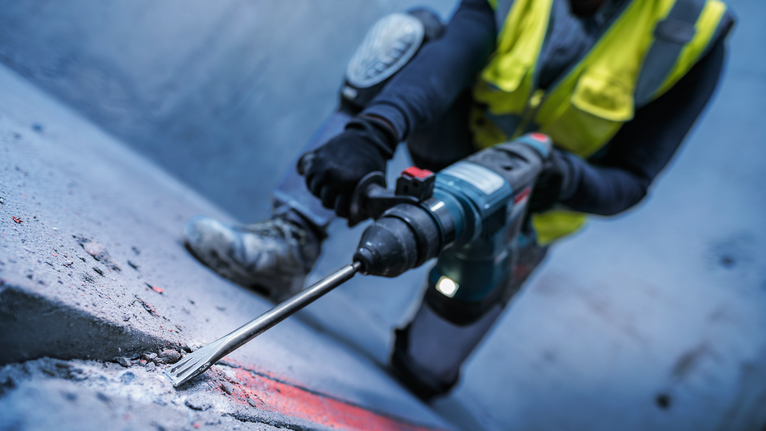 一名配戴安全設備的人員用旋轉錘鑿擊混凝土表面。