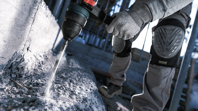 一名配戴安全設備的人員使用旋轉錘在混凝土中鑽孔。
