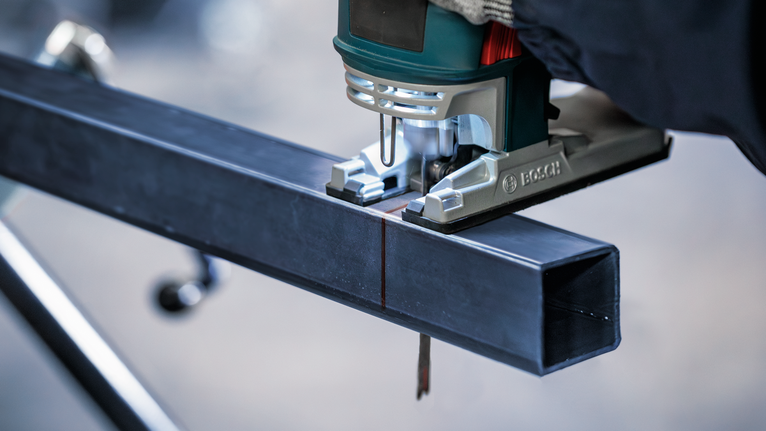 配戴安全設備的人員使用曲線鋸切割金屬梁。