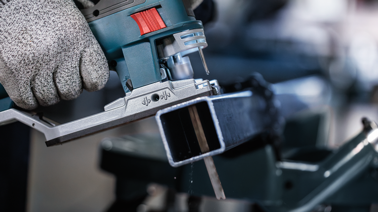 配戴安全設備的人員使用曲線鋸切割金屬梁。