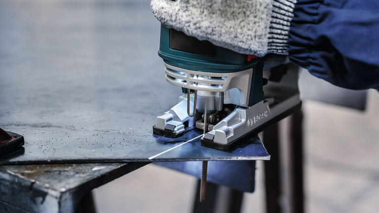 PRO Metal thick and thin T123XF 線鋸片,100 mm,3 件 一名配戴安全設備的人正在用曲線鋸切割一塊金屬板。