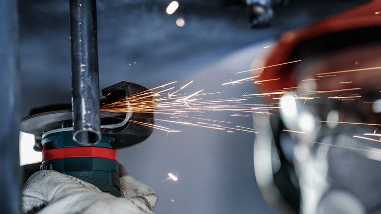 工人配戴安全設備研磨金屬管，產生火花。.