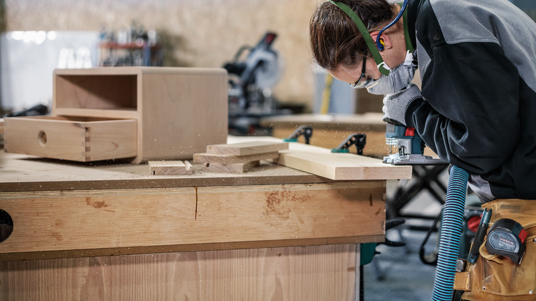 PRO Wood precise T144DP 線鋸片,100 mm,5 片 配戴安全設備的人員使用電動工具在工作台上塑造木板。