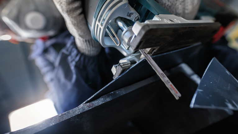 配戴安全設備的人用曲線鋸切割金屬。