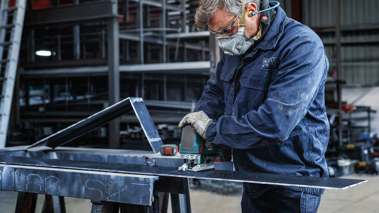 一名配戴安全設備的人員使用電動工具切割金屬板。