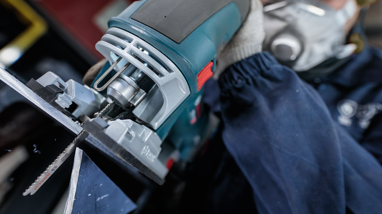 配戴安全設備的人使用曲線鋸切割金屬。