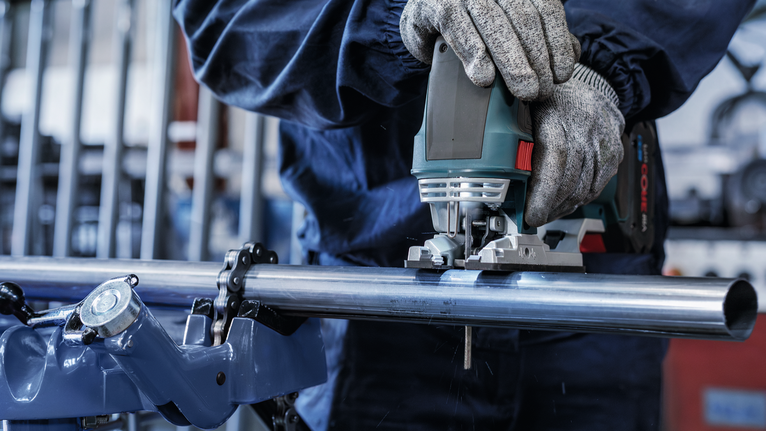 配戴安全設備的人員使用曲線鋸切割金屬管。