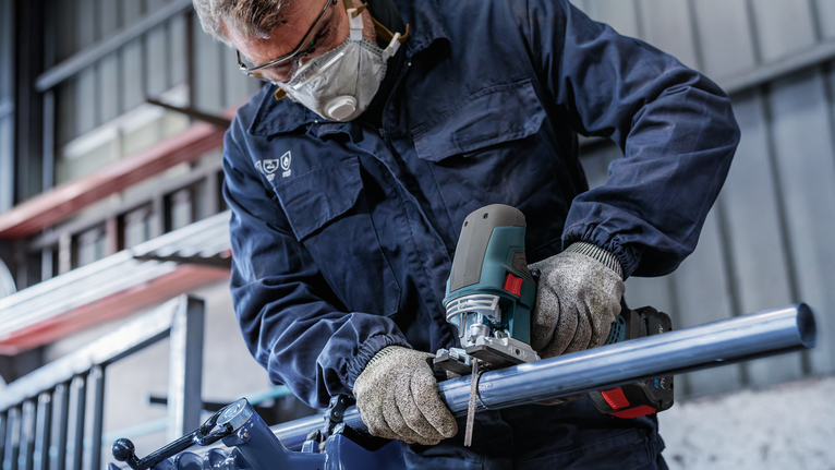 配戴安全設備的人員用曲線鋸切割金屬管。