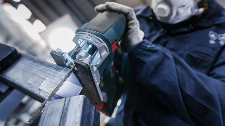 一名配戴安全設備的人員使用往復鋸切割金屬梁。