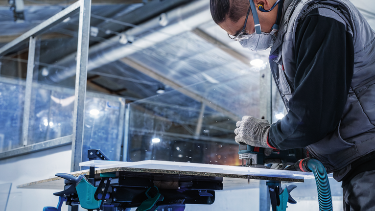 一名配戴安全設備的人員使用電動工具切割木板。