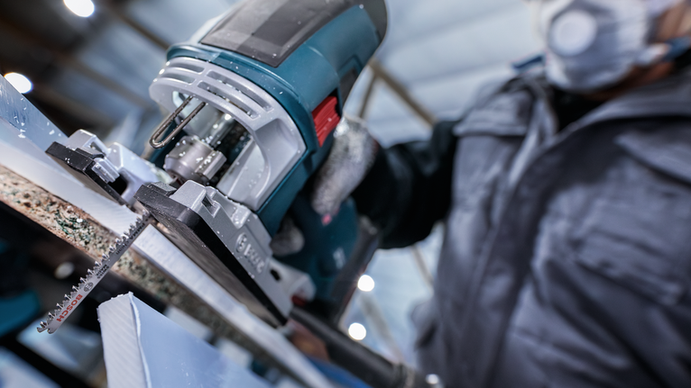 一名配戴安全設備的人使用曲線鋸切割一塊材料。