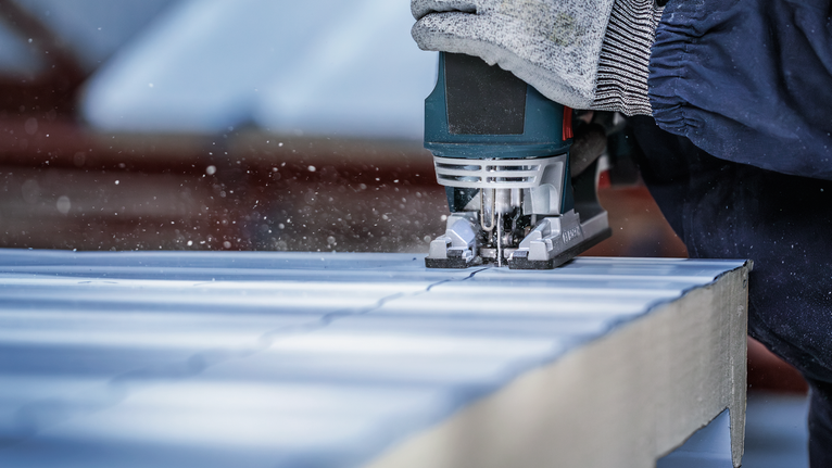 配戴安全設備的人員使用曲線鋸在面板上切割出一條直線。