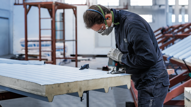 一名配戴安全設備的人員正在使用電動工具切割金屬板。