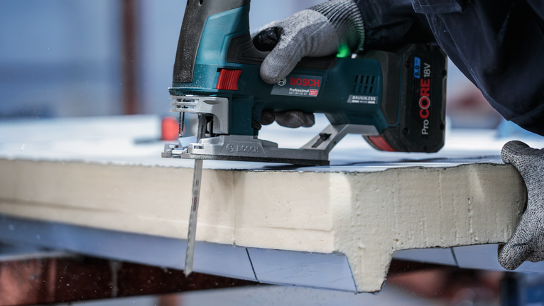 一名配戴安全設備的人員使用無線曲線鋸切割泡棉板。