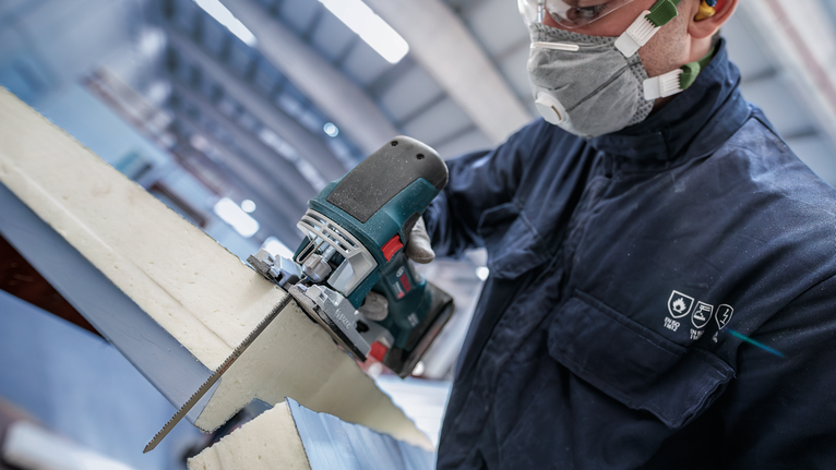 配戴安全設備的人員使用電動曲線鋸切割泡棉絕緣材料。