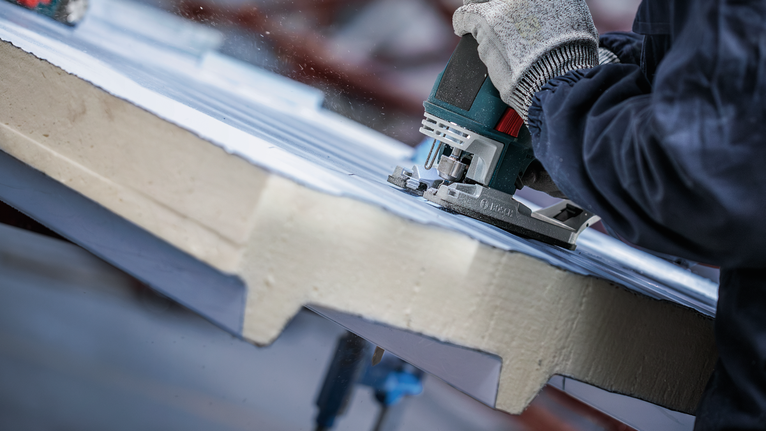 一名配戴安全設備的人員正在用曲線鋸切割絕緣材料。