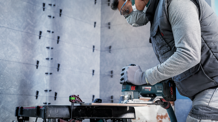 PRO Soft Tile T130RF 線鋸片,83 mm,3 件 一名配戴安全設備的人員使用電鋸在工作台上切割木材。