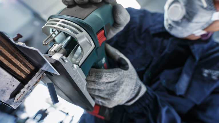 一名配戴安全設備的人員操作電動工具切割金屬片。
