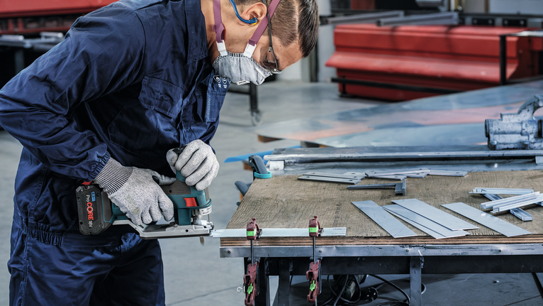 一名配戴安全設備的人員在工作台上用電鋸切割金屬板。