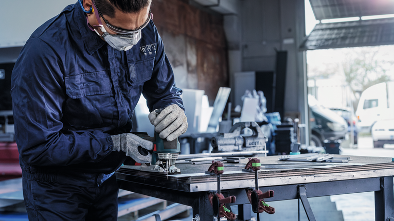 配戴安全設備的人員使用電動工具在工作台上打磨金屬。