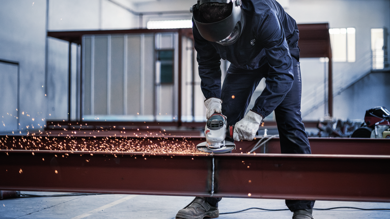 一名佩戴安全設備的人正在研磨金屬梁，產生火花。