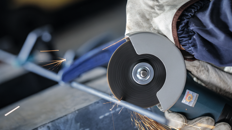 配戴安全設備的人員用切割工具研磨金屬棒。