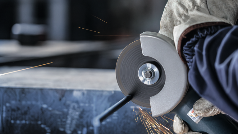 配戴安全設備的人用角磨機切割金屬，產生火花。