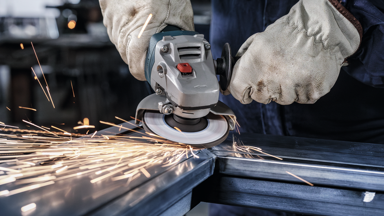 配戴安全設備的人使用角磨機切割金屬，產生火花。.