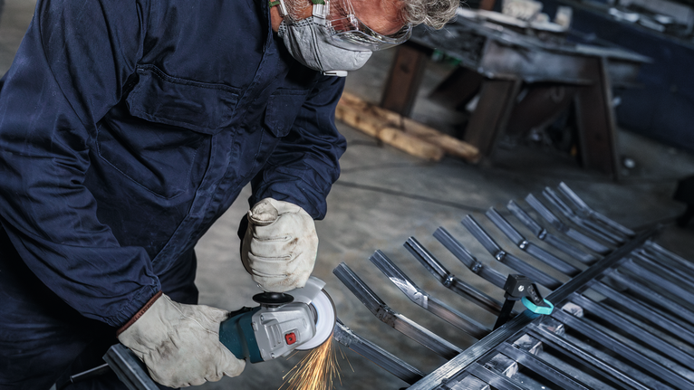 配戴安全設備的人員使用電動工具研磨金屬棒。