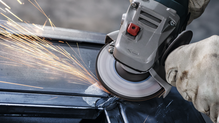 穿著安全設備的人研磨金屬，產生明亮的火花。