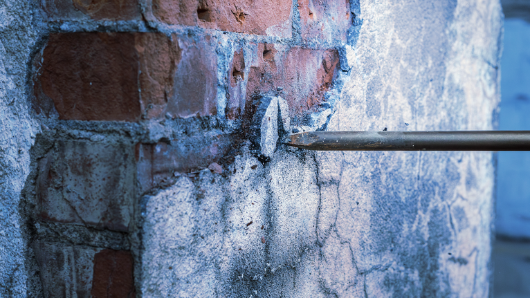 用鑽鑿破壞磚牆上的灰泥。.