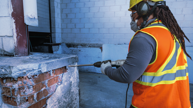 一名穿著安全設備的工人正在混凝土平台上鑽孔。.